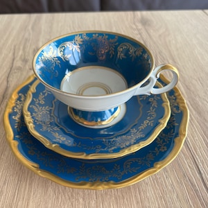 May include: A three-piece tea set featuring a teacup, saucer, and dessert plate. The set has a vibrant blue base with gold floral detailing and trim. The teacup is white inside. A classic and elegant design.