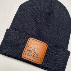 Puede incluir: Un gorro de punto azul marino con un parche de cuero marr&oacute;n. El parche presenta las palabras "MAKE. HEAVEN. CROWDED." en letras blancas. Un estilo de gorro cl&aacute;sico, adecuado para el clima fr&iacute;o.