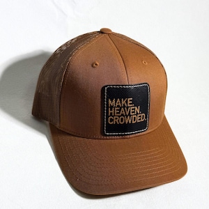 May include: A brown trucker hat with a mesh back and a curved brim. The front features a black square patch with the embroidered text "MAKE. HEAVEN. CROWDED."