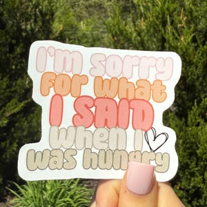 May include: A white sticker with the text "I'm sorry for what I said when I was hungry" in pink, orange, red, and tan bubble letters. A small black heart is next to the word "I".