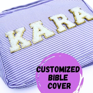 May include: A purple and white striped fabric Bible cover with the name "KARA" in gold letters with white trim. The cover has a pink circle with the text "CUSTOMIZED BIBLE COVER" in black.