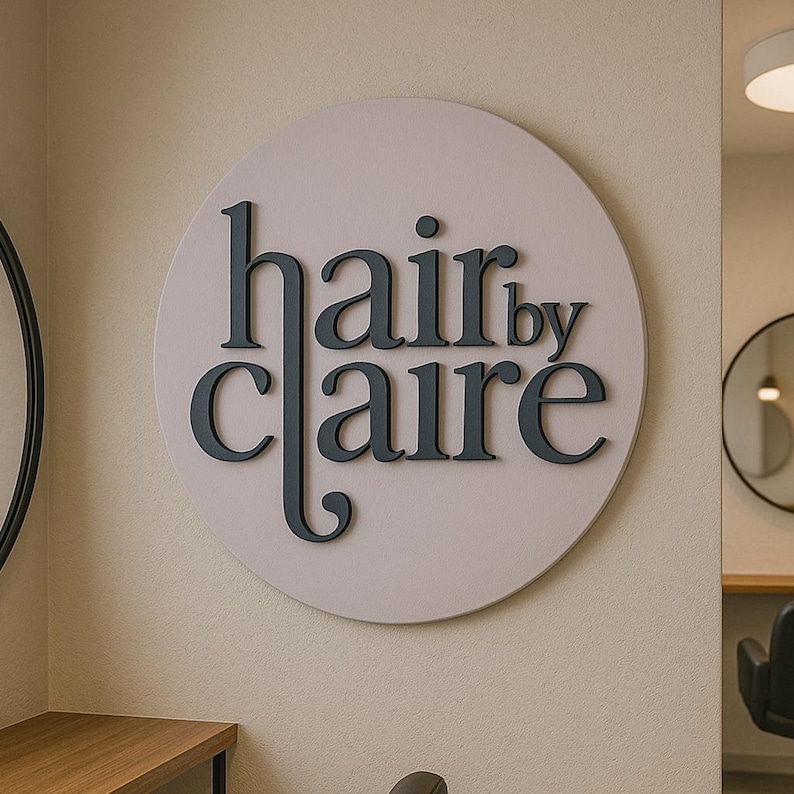 May include: A round, light pink sign with the text "hair by claire" in black lettering.