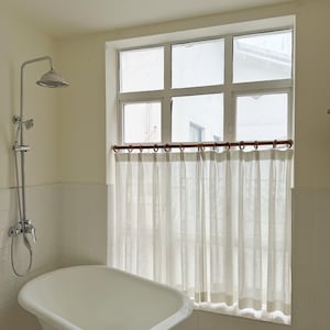 May include: A bathroom featuring a white clawfoot bathtub, a chrome shower, and a window with sheer white curtains. The walls are cream-colored, and the floor has black and white tiles.