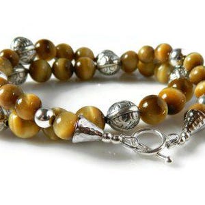 May include: A double-strand bracelet featuring polished golden-brown tiger's eye beads interspersed with round, etched silver-tone metal beads and smooth silver-tone spacers, finished with a silver-tone toggle clasp and a conical end cap.