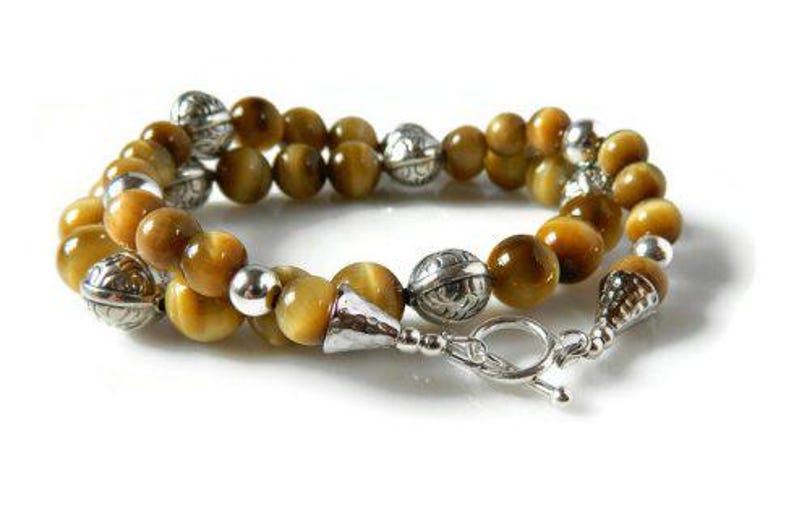 May include: A double-strand bracelet featuring polished golden-brown tiger's eye beads interspersed with round, etched silver-tone metal beads and smooth silver-tone spacers, finished with a silver-tone toggle clasp and a conical end cap.