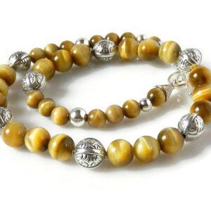 May include: A beaded necklace featuring round, golden-brown tiger's eye gemstones interspersed with polished silver-tone metal beads. The silver beads alternate between smooth, plain spheres and larger, intricately engraved decorative metal spacers.