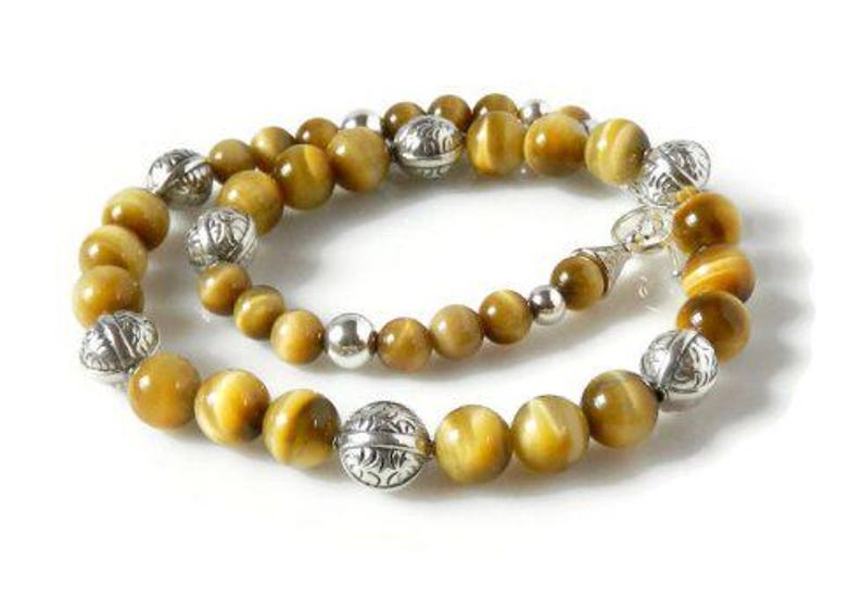 May include: A beaded necklace featuring round, golden-brown tiger's eye gemstones interspersed with polished silver-tone metal beads. The silver beads alternate between smooth, plain spheres and larger, intricately engraved decorative metal spacers.