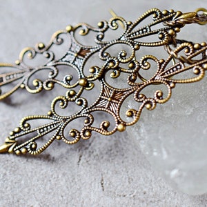 May include: A pair of ornate gold filigree earrings with a delicate, intricate design. The earrings are made of metal and have a vintage look.