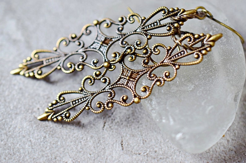 May include: A pair of ornate gold filigree earrings with a delicate, intricate design. The earrings are made of metal and have a vintage look.