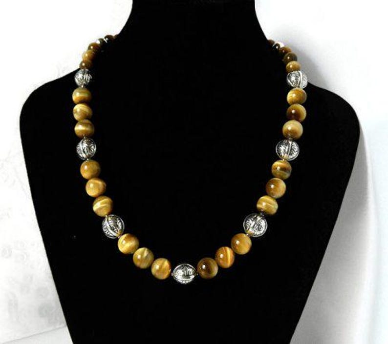 May include: A beaded necklace featuring alternating round, golden-brown tiger's eye gemstones and spherical, silver-toned metal beads with an intricate, embossed floral pattern throughout the entire length of the strand.