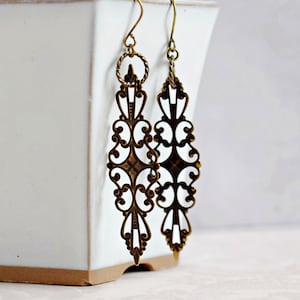 May include: A pair of long, gold-tone earrings with a delicate, intricate filigree design. The earrings are made of metal and have a dangling, drop shape.