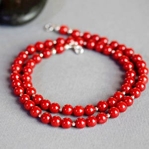 May include: A red beaded necklace with silver clasps. The necklace is made of round beads and is layered twice.
