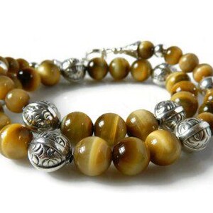 May include: A beaded bracelet featuring round, golden-brown tiger's eye gemstones interspersed with polished, etched silver-tone metal beads. The bracelet is arranged in a circular loop and includes a silver-tone metal clasp mechanism.