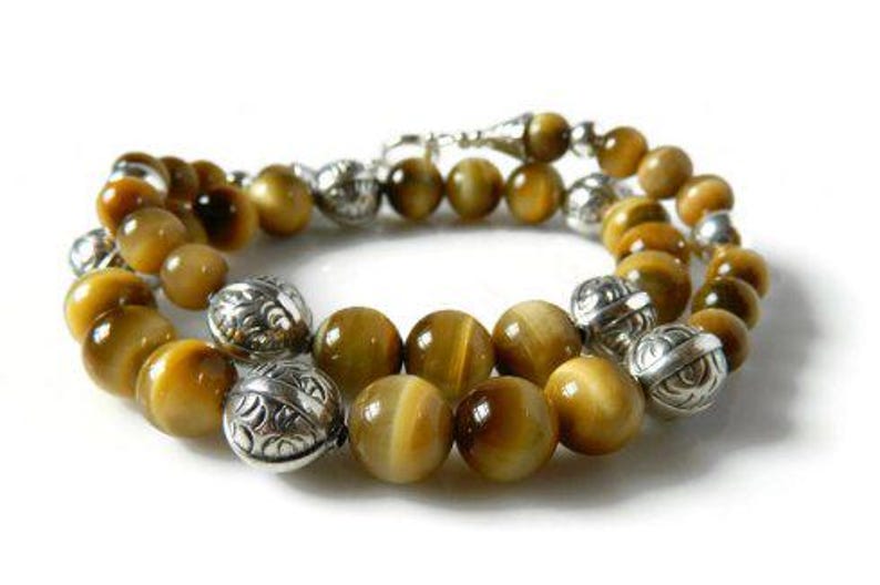 May include: A beaded bracelet featuring round, golden-brown tiger's eye gemstones interspersed with polished, etched silver-tone metal beads. The bracelet is arranged in a circular loop and includes a silver-tone metal clasp mechanism.