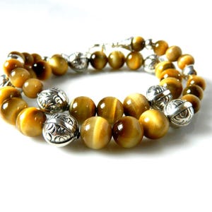 May include: A beaded bracelet featuring round, golden-brown tiger's eye gemstones interspersed with polished silver-toned metal beads. The metal beads are spherical and decorated with intricate, engraved patterns throughout their surface.