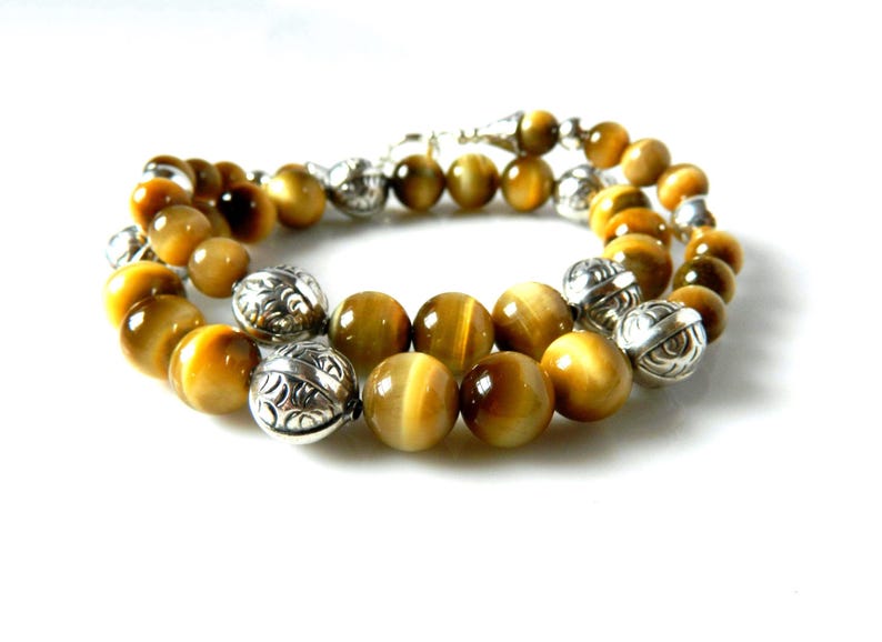 May include: A beaded bracelet featuring round, golden-brown tiger's eye gemstones interspersed with polished silver-toned metal beads. The metal beads are spherical and decorated with intricate, engraved patterns throughout their surface.