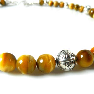 May include: A beaded necklace featuring round, polished golden-brown tiger's eye gemstones alternating with spherical, silver-toned metal beads that have an intricate, engraved leaf-like pattern throughout the surface of the metal.