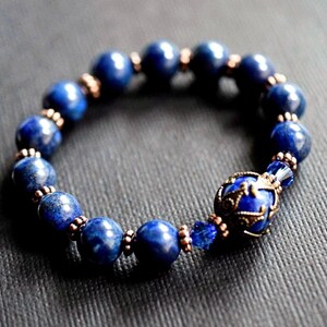 A blue lapis lazuli beaded bracelet with a copper and lapis lazuli charm. The bracelet is made with round beads and has a copper clasp.
