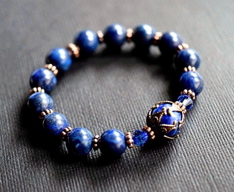A blue lapis lazuli beaded bracelet with a copper and lapis lazuli charm. The bracelet is made with round beads and has a copper clasp.