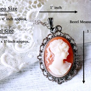 May include: A silver cameo pendant with a red and white cameo featuring a woman's profile. The pendant is 1 1/2 inches tall and 1 inch wide. The cameo is 1 inch tall and 3/4 inch wide.