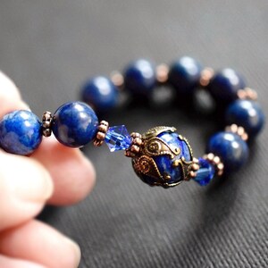 A blue lapis lazuli beaded bracelet with a copper and gold filigree charm. The bracelet has a blue crystal bead and copper spacers.