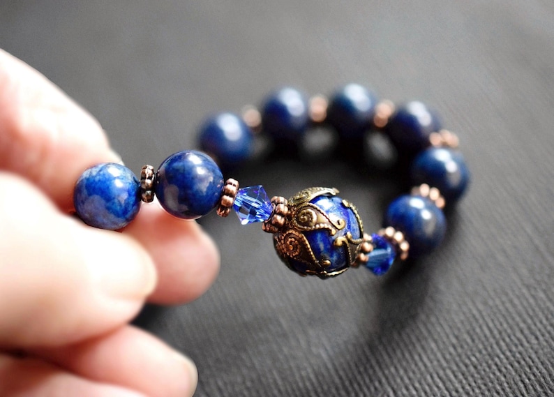 A blue lapis lazuli beaded bracelet with a copper and gold filigree charm. The bracelet has a blue crystal bead and copper spacers.
