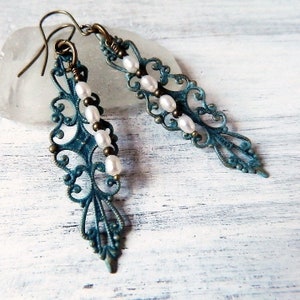 May include: Teal blue filigree earrings with white pearl beads hanging from the bottom. The earrings have a vintage style.