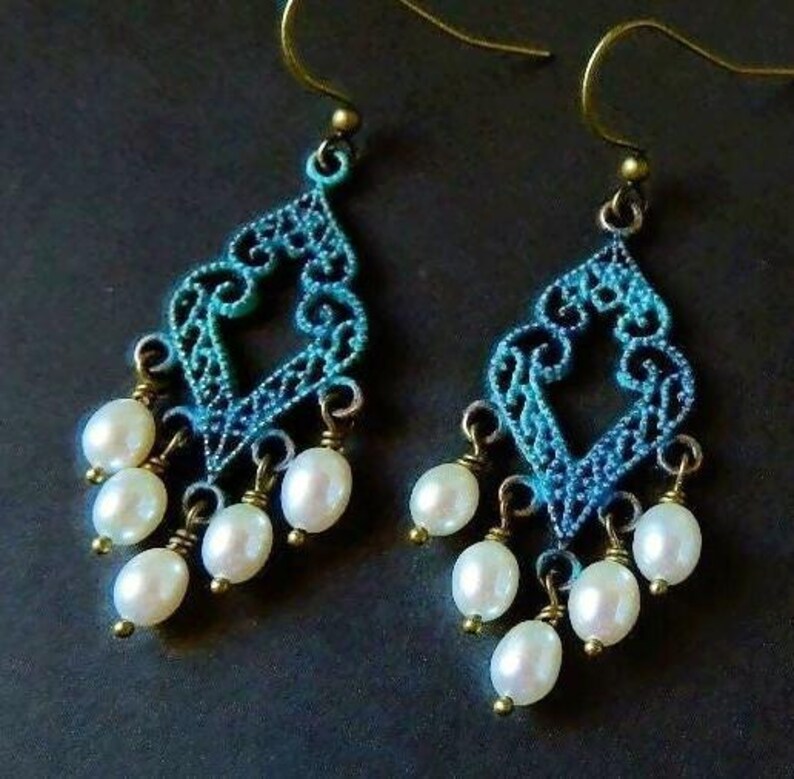 May include: A pair of dangle earrings with a blue and green filigree design and white pearl accents.