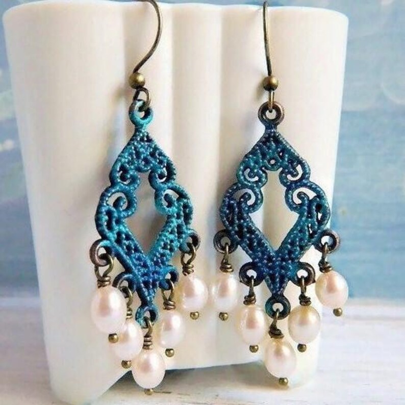 May include: A pair of dangle earrings with a blue and green filigree design and white pearl accents.