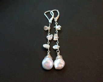 May include: A pair of long drop earrings featuring silver-toned metal chains adorned with small, irregular white pearls. Each earring terminates in a larger, teardrop-shaped pearl wrapped in silver wire, suspended from a lever-back closure.