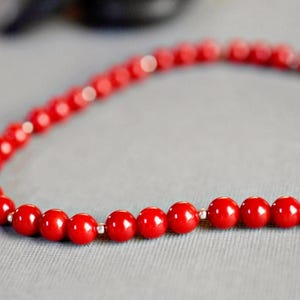 May include: A red beaded necklace with silver accents. The beads are round and smooth, and the necklace is strung on a silver chain.