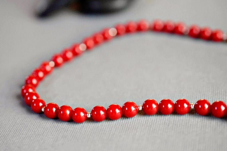 May include: A red beaded necklace with silver accents. The beads are round and smooth, and the necklace is strung on a silver chain.