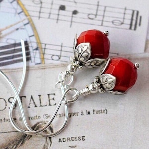 May include: A pair of silver earrings with red faceted glass beads and silver floral accents.