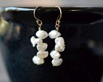 May include: A pair of gold earrings with a cluster of white baroque pearls hanging from each earring.