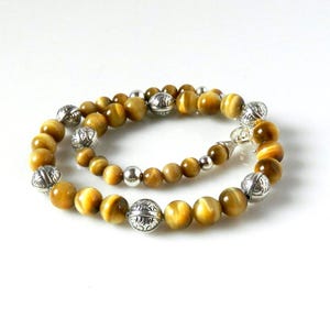 May include: A beaded necklace featuring round, golden-brown tiger's eye gemstones interspersed with polished silver-toned metal beads. The necklace includes ornate, etched silver-toned spherical beads and smaller, smooth silver-toned spacer beads.