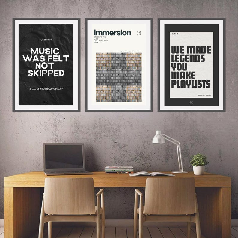 May include: Three black framed posters with white text on a textured background. The posters are hanging on a grey wall. The left poster says "Music was felt not skipped" and has the text "No legends in your discover weekly". The middle poster says "Immersion" and has the text "Dive into the sound, let the world fade". The right poster says "We made legends you make playlists".