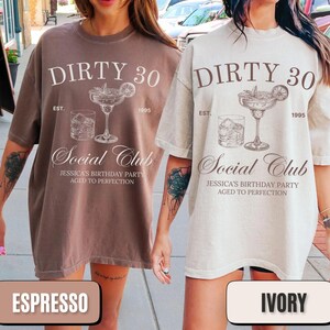 Pu&ograve; includere: Due t-shirt oversize con il testo "Dirty 30 Est. 1995 Social Club Jessica's Birthday Party Aged to Perfection" stampato su di esse. Le magliette sono nei colori espresso e avorio.