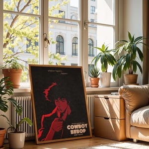 Puede incluir: Un póster enmarcado con una ilustración roja y negra de un personaje de la serie de anime Cowboy Bebop. El póster está en una habitación con plantas y una ventana que da a un edificio. El póster dice "Cowboy Bebop".