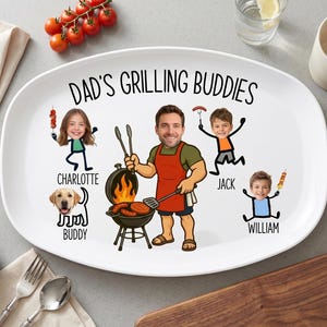 May include: White oval platter with the text "Dad's Grilling Buddies" and cartoon illustrations of a man grilling, three children, and a dog. The platter has a grey background with tomatoes, avocado, and a mug.