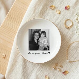 May include: White ceramic trinket dish with a gold rim, featuring a black and white photo of a mother and child. The dish has the handwritten text "Love you, Mom" and a heart symbol.