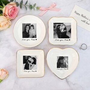 May include: Four white ceramic trinket dishes in round, square, and heart shapes, each with a gold rim and a black and white photo. The dishes have the text "Love you, Mom" and a heart. A card reads "Happy Mother's Day with love."
