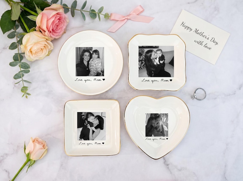 May include: Four white ceramic trinket dishes in round, square, and heart shapes, each with a gold rim and a black and white photo. The dishes have the text "Love you, Mom" and a heart. A card reads "Happy Mother's Day with love."
