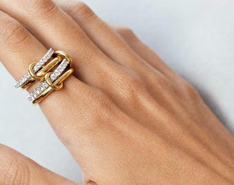 May include: A gold-toned ring with a knot design, adorned with rows of small, sparkling stones. The ring is worn on a hand, showcasing its intricate details and elegant style. The ring's design features a double-banded structure.