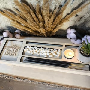 Puede incluir: Una bandeja de madera clara con compartimentos para incienso, una vela y piedras pequeñas. La bandeja tiene el nombre "Davis" y un diseño floral grabado. También hay una pequeña planta en maceta y varillas de incienso.