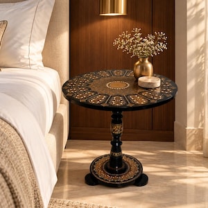 May include: A round black side table with an intricate gold and white inlaid floral pattern on the top and base. The table features a central pedestal column with decorative gold accents and sits on a circular base with matching ornate detailing.