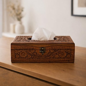 Op de afbeelding: Een rechthoekige houten tissuebox met ingewikkelde bloemsnijwerk en een scharniersluiting. De doos heeft een warme bruine kleur en bevat een stapel witte tissues. Het ontwerp heeft gedetailleerde patronen.