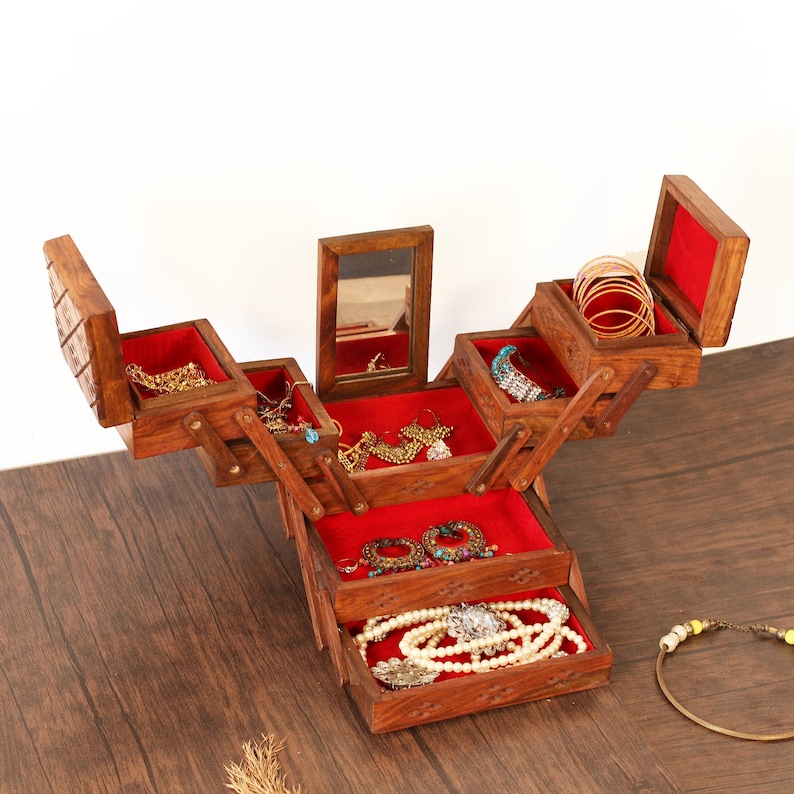 May include: A wooden jewelry box with multiple compartments, lined with red velvet. The box is open, displaying various necklaces, bracelets, and earrings. A small mirror is visible inside the box. The box is made of dark wood.