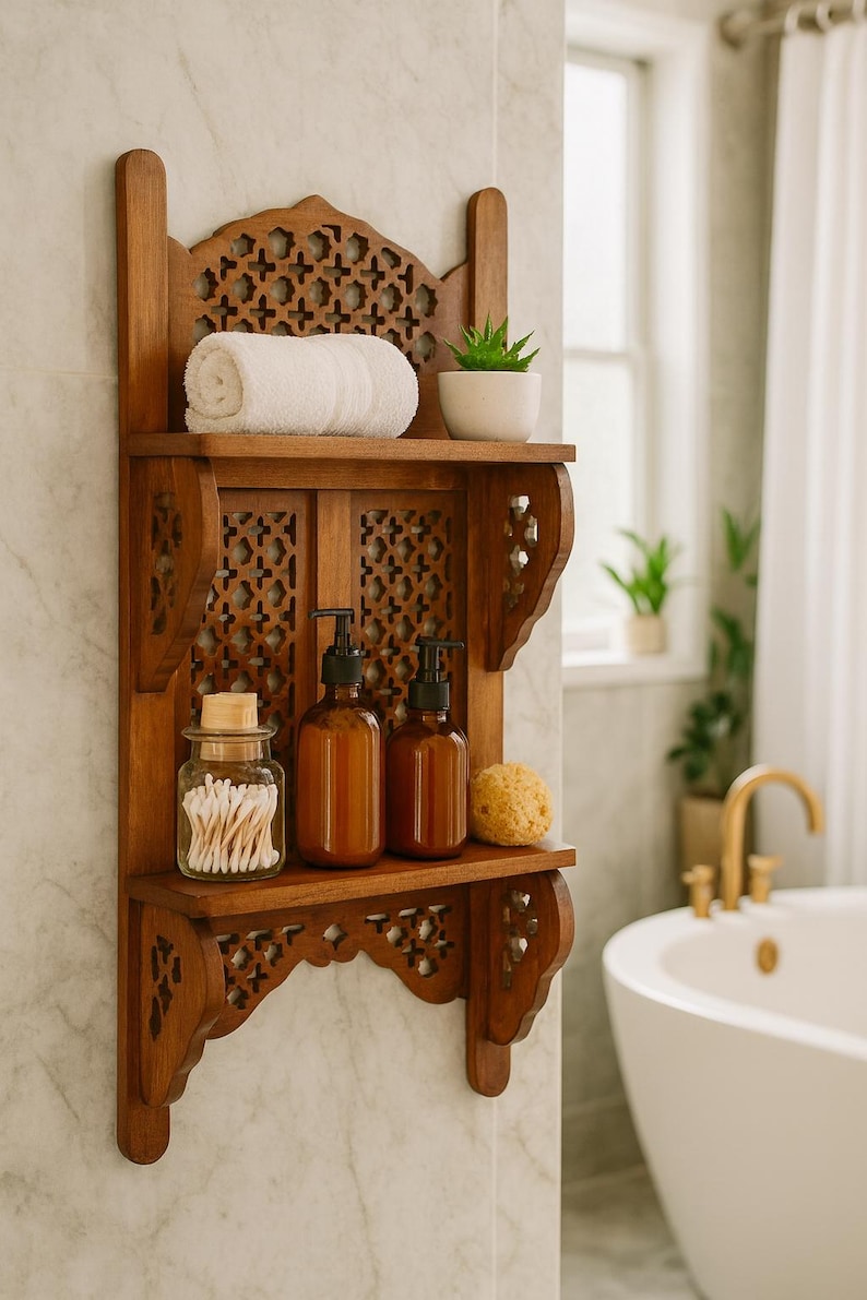 Puede incluir: Estanter&iacute;a de ba&ntilde;o de madera con detalles tallados. La estanter&iacute;a contiene una toalla blanca enrollada, una peque&ntilde;a planta en maceta, dos botellas con bomba marrones, un tarro de bastoncillos de algod&oacute;n y una esponja natural. La estanter&iacute;a est&aacute; montada en una pared de baldosas de m&aacute;rmol.