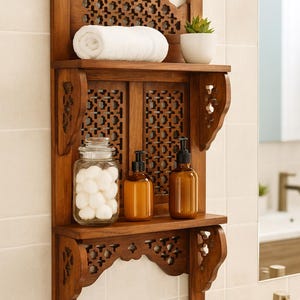 Puede incluir: Estanter&iacute;a de ba&ntilde;o de madera con intrincados detalles tallados. Contiene una toalla blanca enrollada, una peque&ntilde;a planta en maceta, dos botellas &aacute;mbar con dispensador y un tarro de bolas de algod&oacute;n. La estanter&iacute;a est&aacute; montada en una pared alicatada.