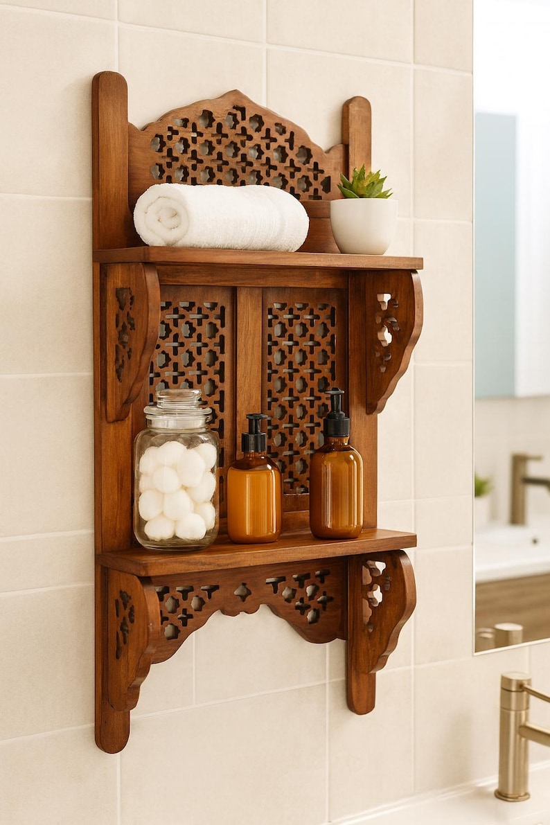 Puede incluir: Estanter&iacute;a de ba&ntilde;o de madera con intrincados detalles tallados. Contiene una toalla blanca enrollada, una peque&ntilde;a planta en maceta, dos botellas &aacute;mbar con dispensador y un tarro de bolas de algod&oacute;n. La estanter&iacute;a est&aacute; montada en una pared alicatada.